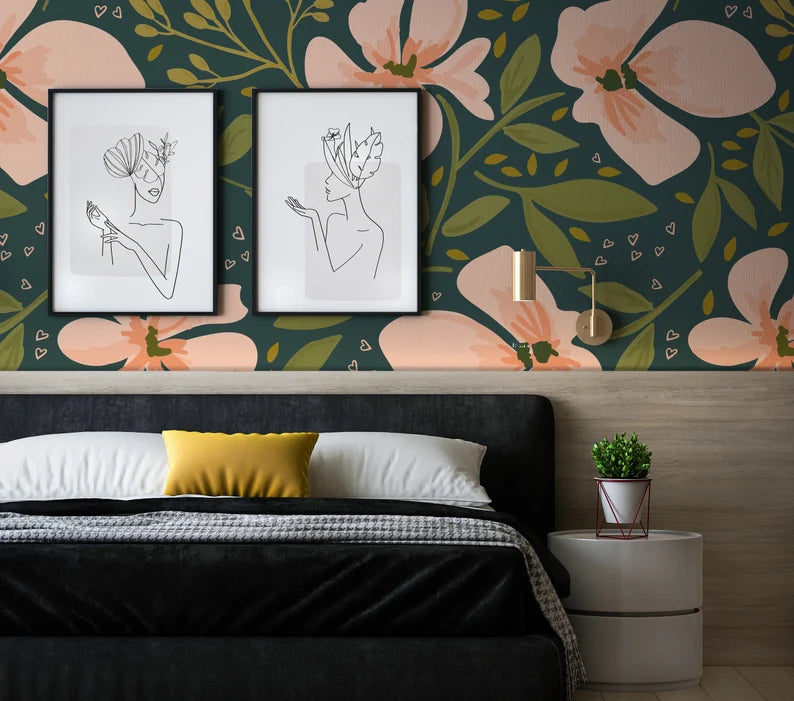 A contemporary bedroom with 'Floral Love Watercolour Wallpaper' in vibrant hues, showcasing oversized pink flowers and lush greenery on a dark background, accented by modern line art portraits above a plush bed with a bold yellow pillow.