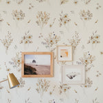 A charming interior wall adorned with 'Meadow Muse Wallpaper', interspersed with wooden frames of artwork, complemented by a vintage gold reading lamp, creating a cozy and artistic atmosphere.
