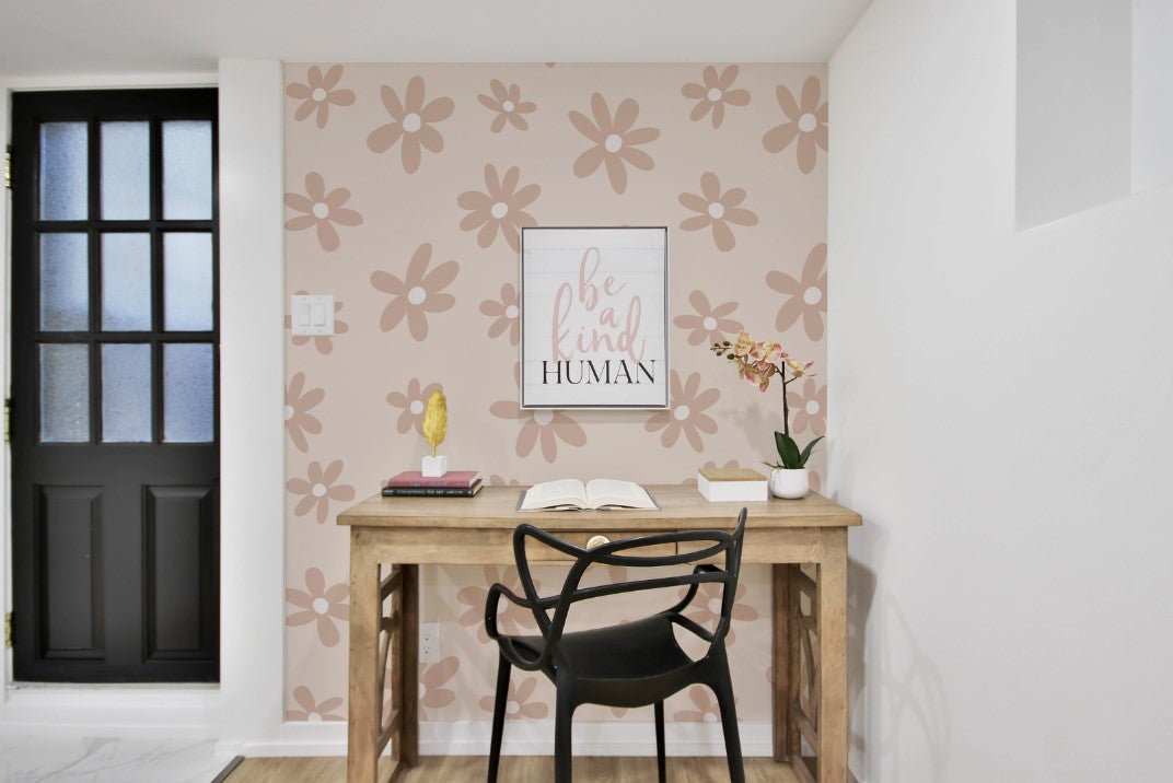 A minimalist workspace with a wooden desk, a black chair, and a "be kind human" framed print. The wall behind is decorated with Simple Mauve Floral Wallpaper featuring large, soft mauve flowers on a light beige background, adding a cozy and inviting feel to the room.