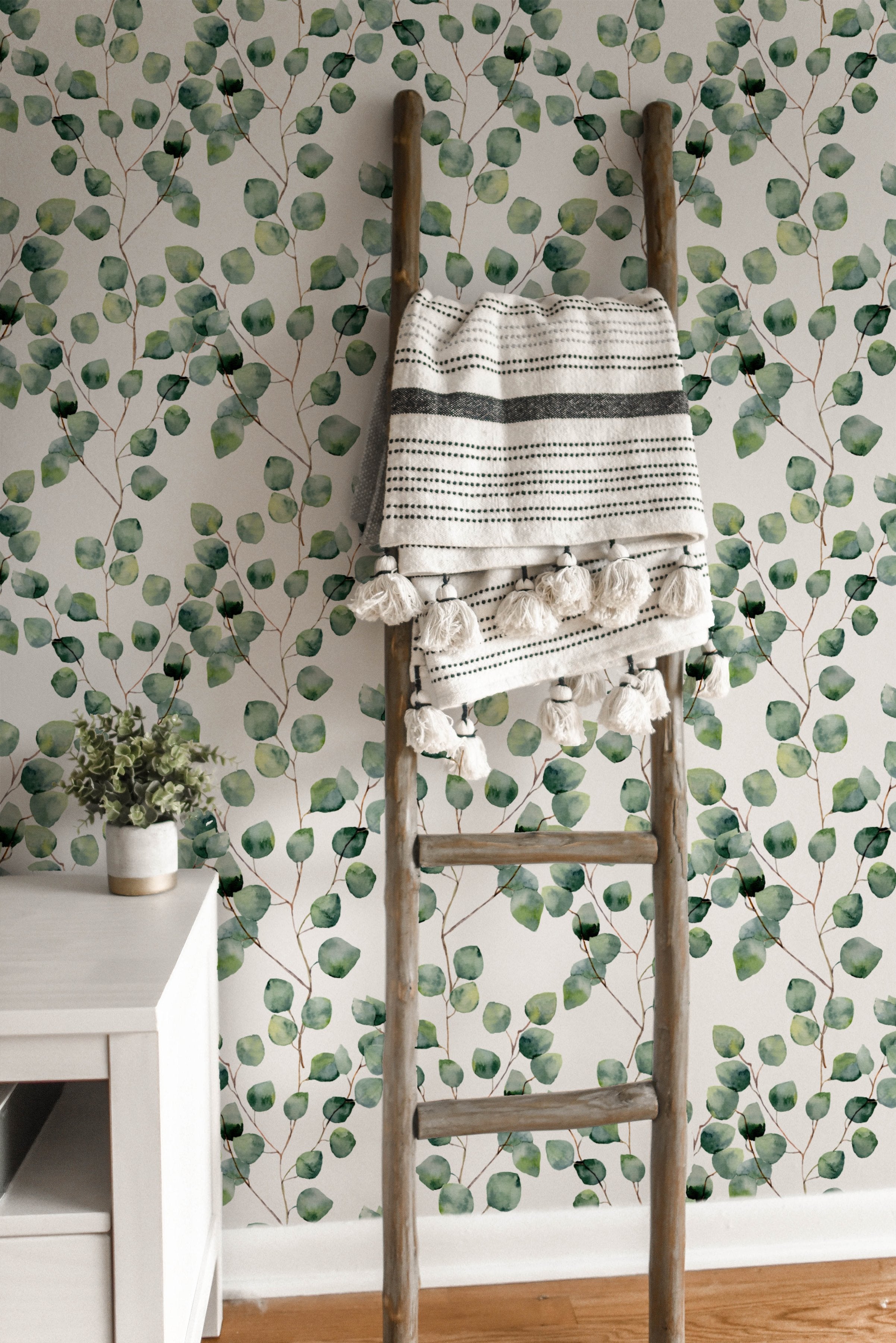 A rustic wooden ladder draped with a patterned throw, standing against the Watercolour Floral Wallpaper - Eucalyptus, complementing the wallpaper's organic feel with natural textures.