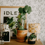 A vibrant home office setup decorated with Watercolour Spring Leaf Wallpaper, complemented by green houseplants and a modern lamp with a patterned shade, enhancing the room's lively yet peaceful nature