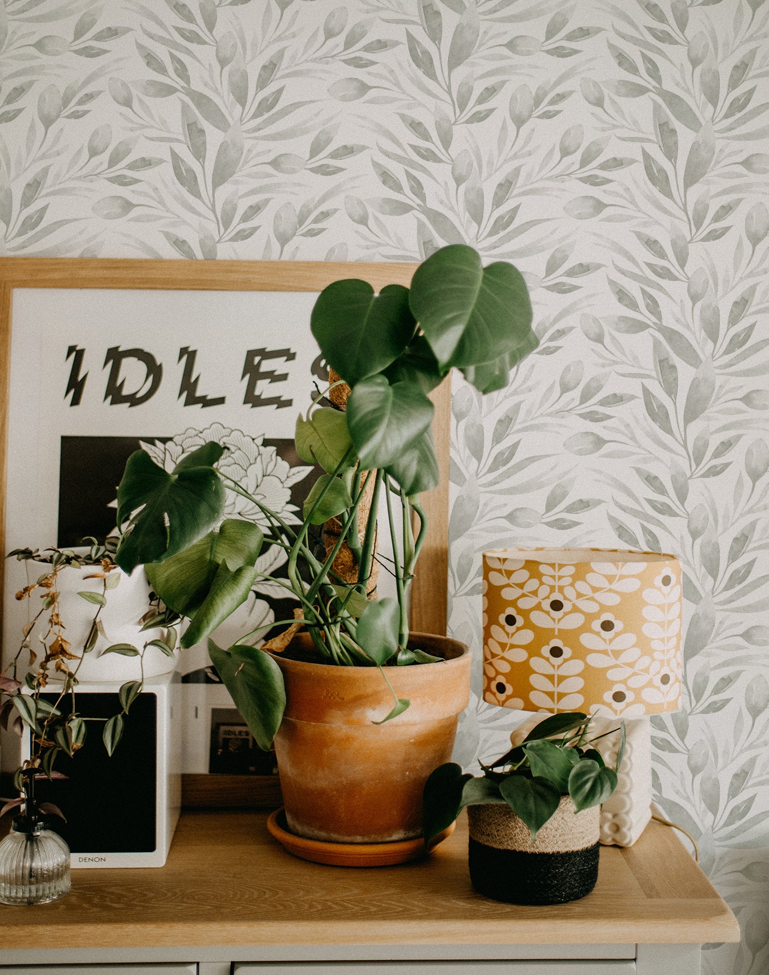 A vibrant home office setup decorated with Watercolour Spring Leaf Wallpaper, complemented by green houseplants and a modern lamp with a patterned shade, enhancing the room's lively yet peaceful nature