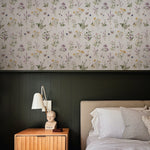 A bedroom wall covered in Midsummer Watercolour Bouquet Wallpaper showcasing a scattered arrangement of watercolor wildflowers. Above a dark green wainscoting, the wallpaper blooms with a mix of gentle purples, sunny yellows, and soft pinks, bringing a touch of nature's serenity indoors.