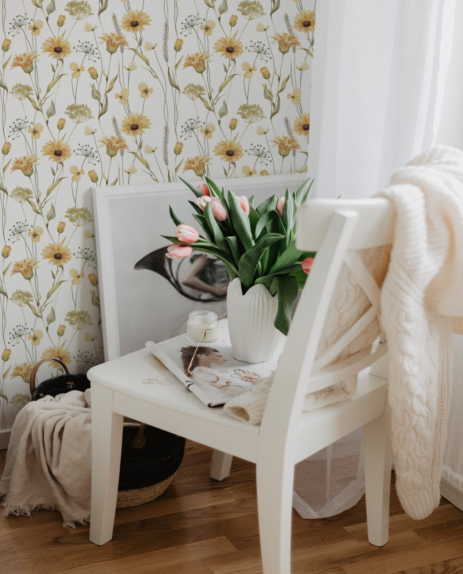 A cozy corner featuring the Watercolour Sunflower Wallpaper adorned with charming sunflowers and delicate flora in watercolor tones of yellow and green. A white chair with a vase of vibrant tulips adds a fresh touch to the inviting scene.