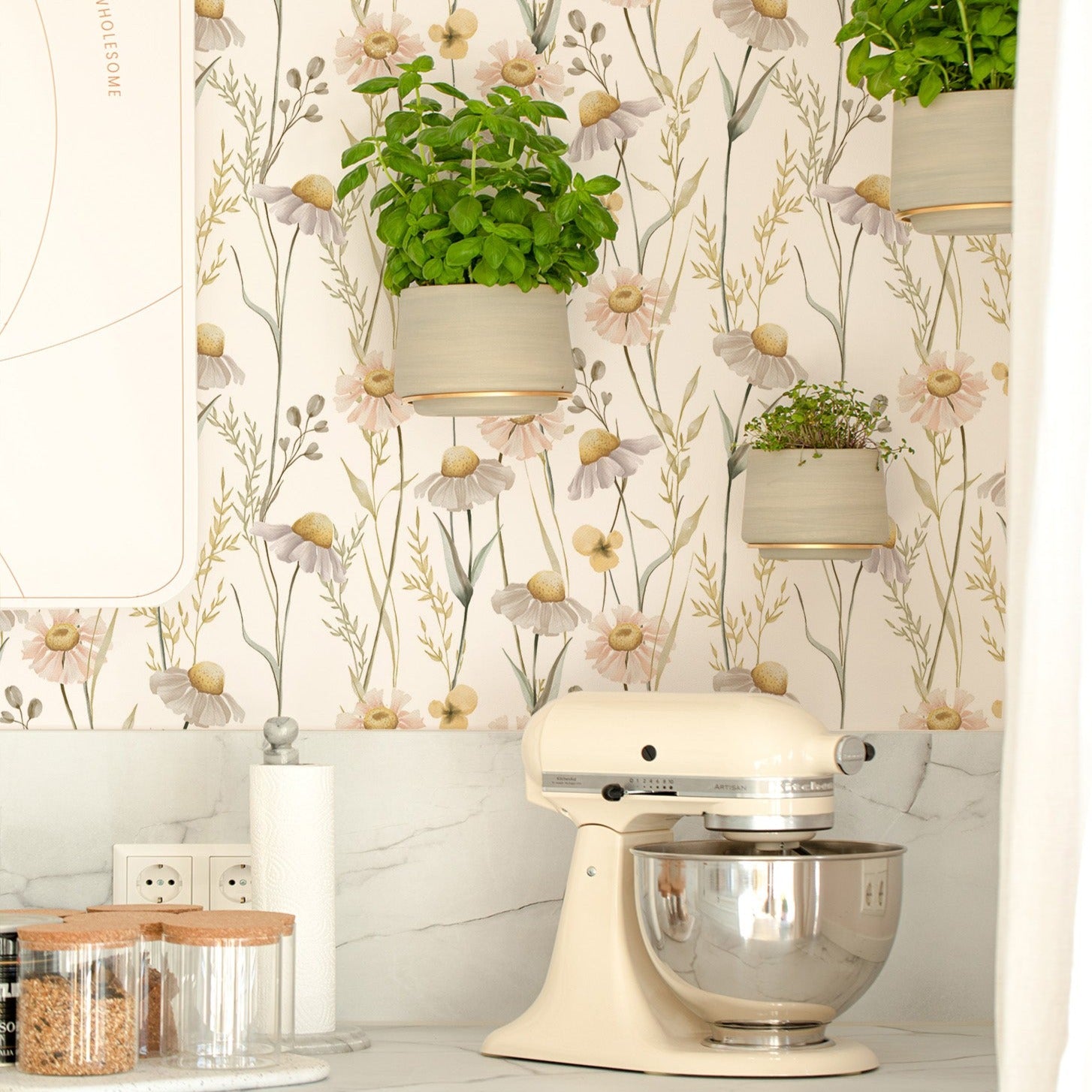 A well-lit kitchen corner featuring the Watercolour Daisy Wallpaper, which brings a light and airy floral aesthetic to the space. Hanging plants and a stylish kitchen mixer on the countertop reflect a blend of functionality and natural beauty.