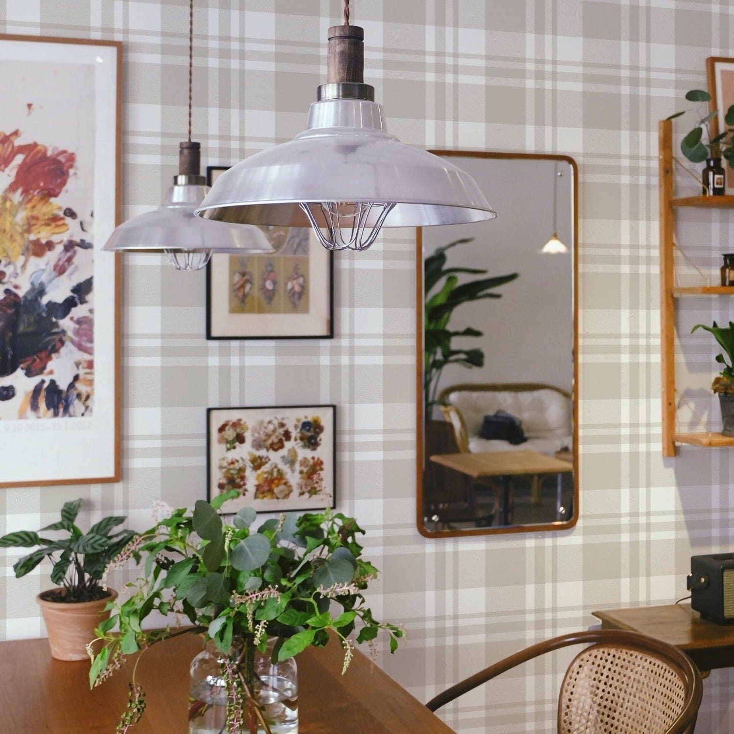  A cozy dining room scene featuring the Plaid Wallpaper - Linen on the walls, lending a comforting and stylish backdrop to the room. The linen-colored plaid pattern adds a touch of rustic charm to the space, harmoniously complementing the wooden furniture, industrial-style pendant lamps, and eclectic wall art and mirrors, creating an inviting space that feels like home.