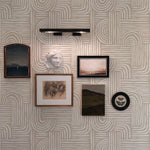 An interior wall features 'Neutral Geometric Wallpaper' with an array of organic, linear geometric patterns in muted beige and white. Various framed artworks and a modern black wall lamp enhance the wallpaper's contemporary aesthetic