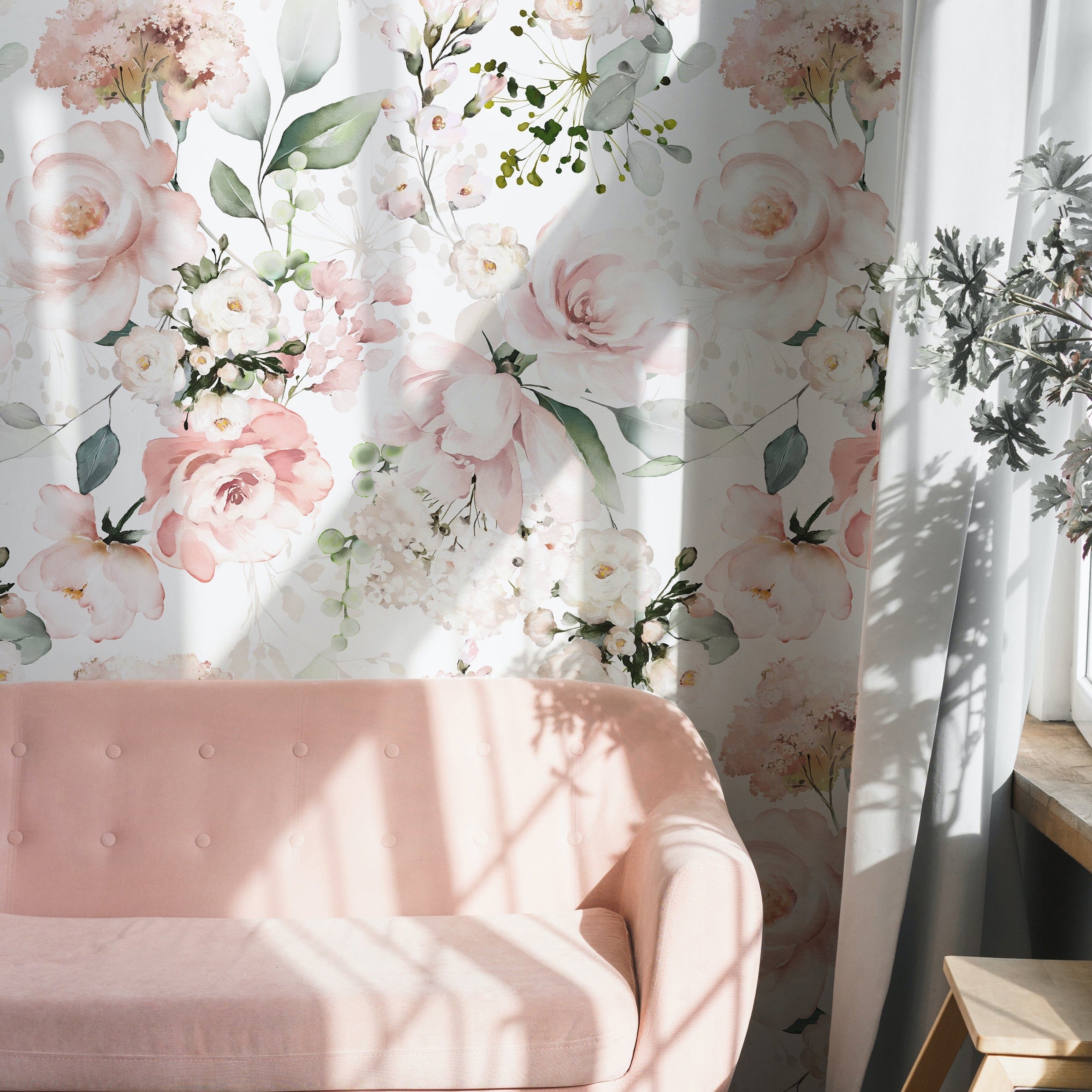 A chic living space accented with the Pink Floral and Herbs Wallpaper - 50", which adorns the wall with its lush, watercolor-style blooms and foliage. A plush pink sofa is positioned against the wallpaper, basking in the natural light that filters through a window, highlighting the soft, pastel colors of the floral pattern.