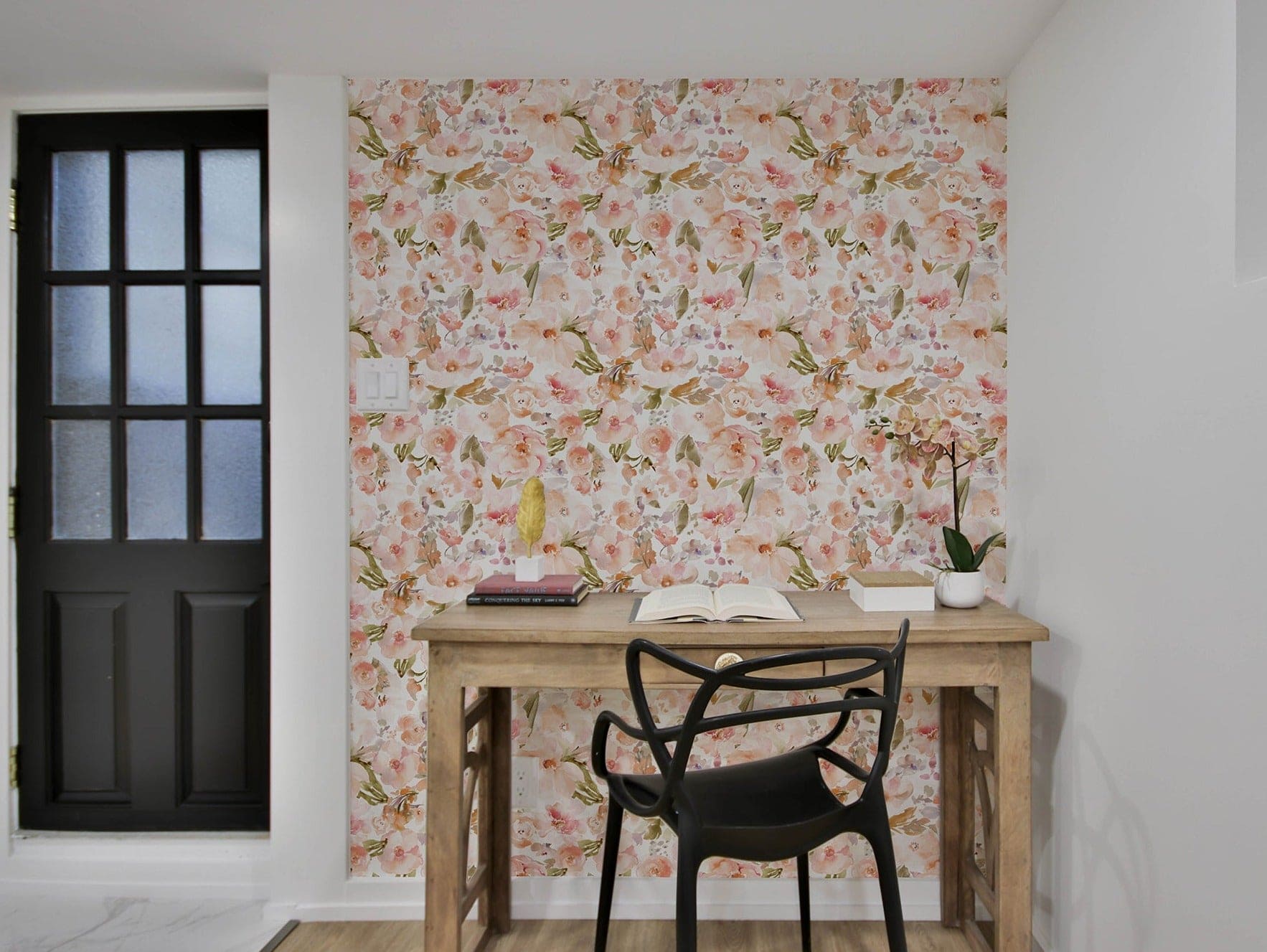 Study area with Watercolour Floral Wallpaper, showcasing a vibrant pattern of peach, pink, and green watercolor flowers on a white background. The wallpaper adds a fresh and lively touch to the space, complemented by a wooden desk and black chair.