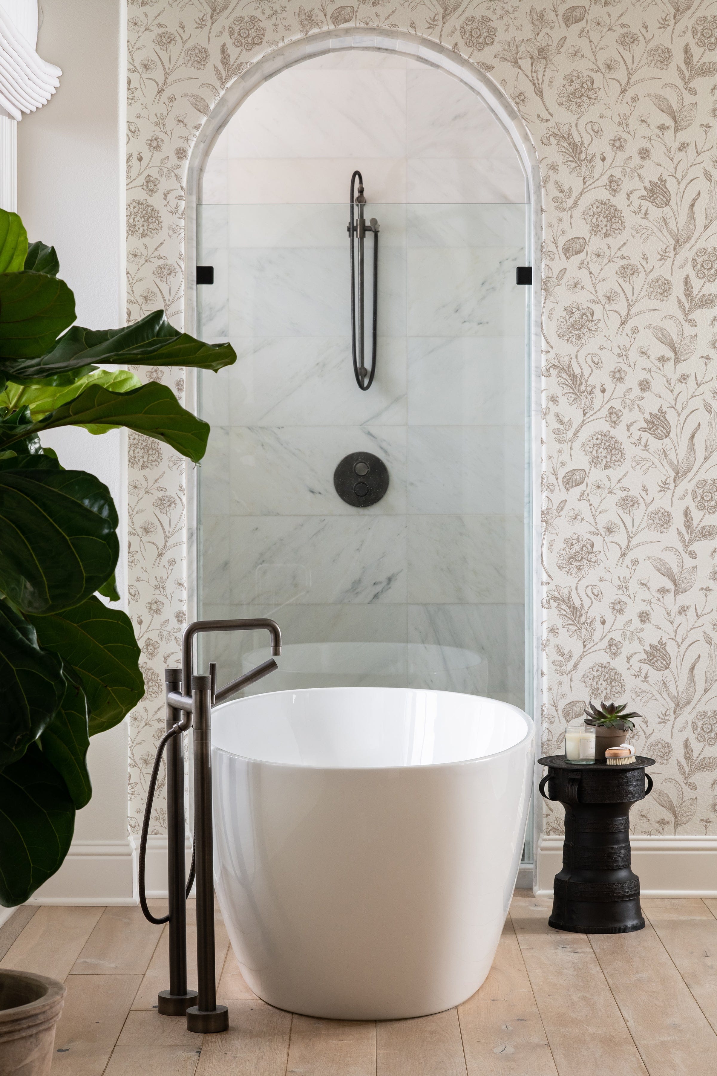 A modern bathroom combines contemporary design with classical elements, featuring Toile De Jouy Floral Wallpaper alongside a sleek white freestanding tub. The floral wallpaper adds a touch of traditional elegance to the space.