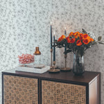 A stylish console table with decorative items against a wall covered in elegant monochrome wallpaper. The wallpaper features a delicate black and white floral pattern, adding a touch of sophistication to the space. The console table is adorned with a vase of orange roses, candles, and a tray, enhancing the elegant ambiance.