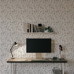 A modern workspace with a desk and computer set against a wall covered in elegant monochrome wallpaper. The wallpaper features a delicate black and white floral pattern, adding a touch of sophistication and style to the space. The desk is adorned with a lamp, a clock, and a vase, creating a clean and organized look