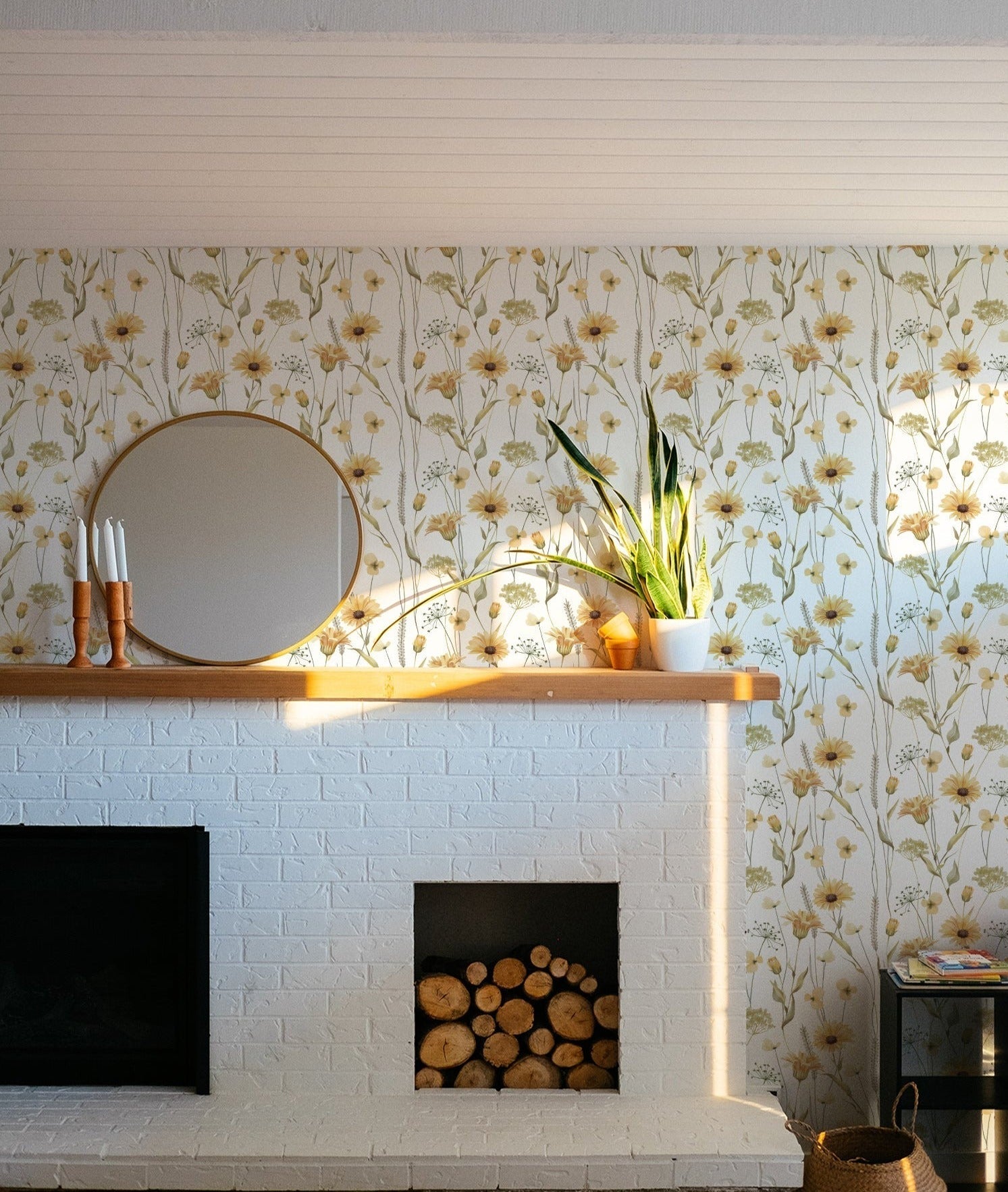 A living space brightened by the Watercolour Sunflower Wallpaper, which provides a joyful backdrop to a white-painted brick fireplace and mantel decorated with candles and a houseplant, reflecting a homely and natural ambiance.