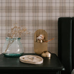 A minimalist setting with a modern black bedside table against Winter Plaid Wallpaper. The plaid design combines classic lines and warm neutral tones that add texture and a welcoming feel to the space, complemented by simple, elegant decor items on the table.