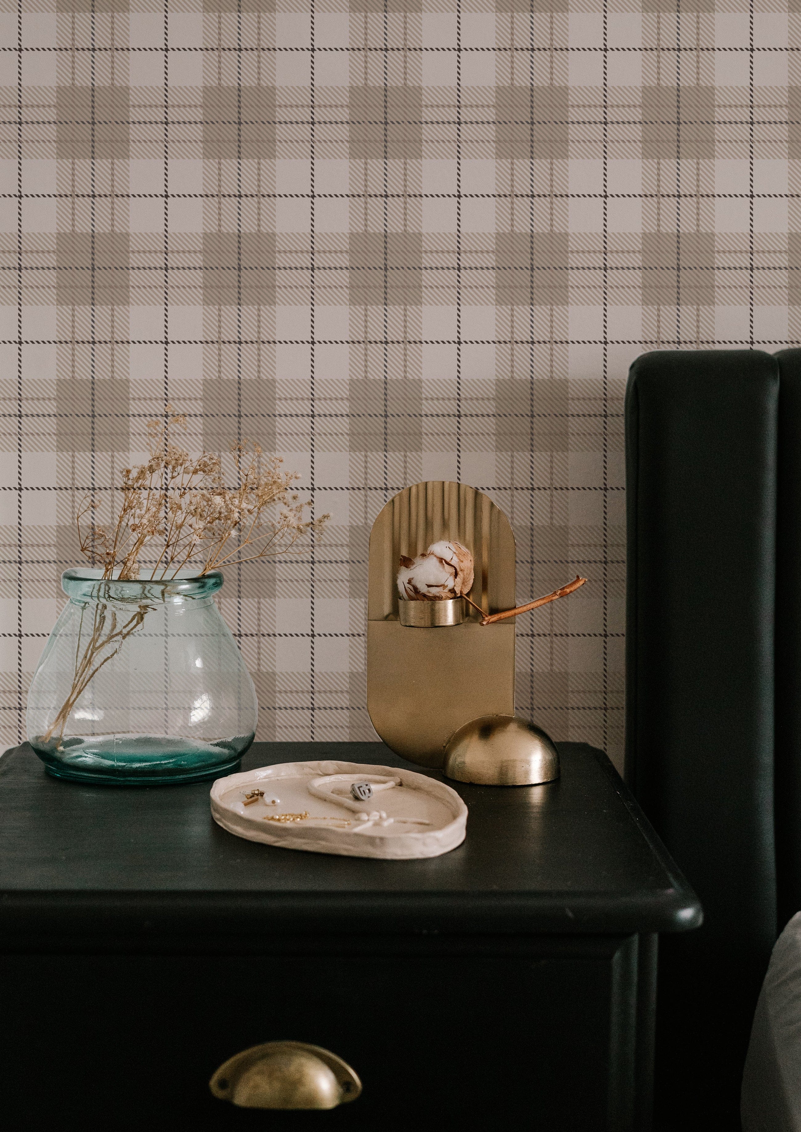 A minimalist setting with a modern black bedside table against Winter Plaid Wallpaper. The plaid design combines classic lines and warm neutral tones that add texture and a welcoming feel to the space, complemented by simple, elegant decor items on the table.