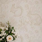 Close-up view of wallpaper with a "Woodland Creatures" theme, showcasing detailed pencil sketches of rabbits, hedgehogs, and squirrels surrounded by plants, mushrooms, and flowers in a soft, neutral palette, giving a tranquil and naturalistic feel to the wall.